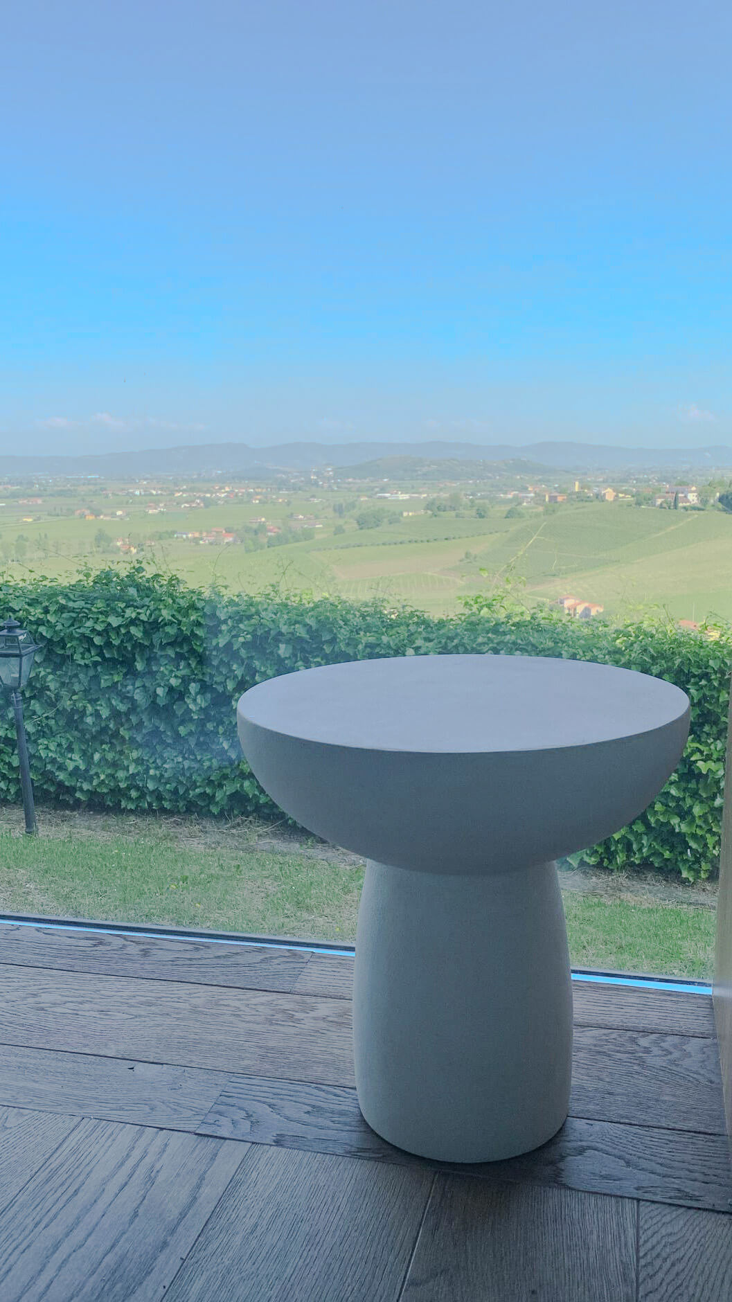 table basse ou d'appoint design en micro ciment mortex® de couleur naturel BM01 devant une baie vitrée avec une vue magnifique, livrée chez une cliente en italie